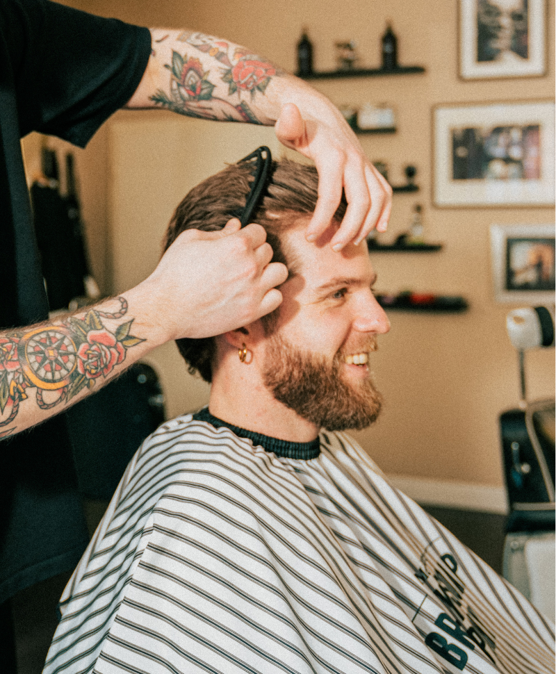 Fröhlicher Mann bekommt im Barbershop einen frischen Haarschnitt von einem tätowierten Barber.