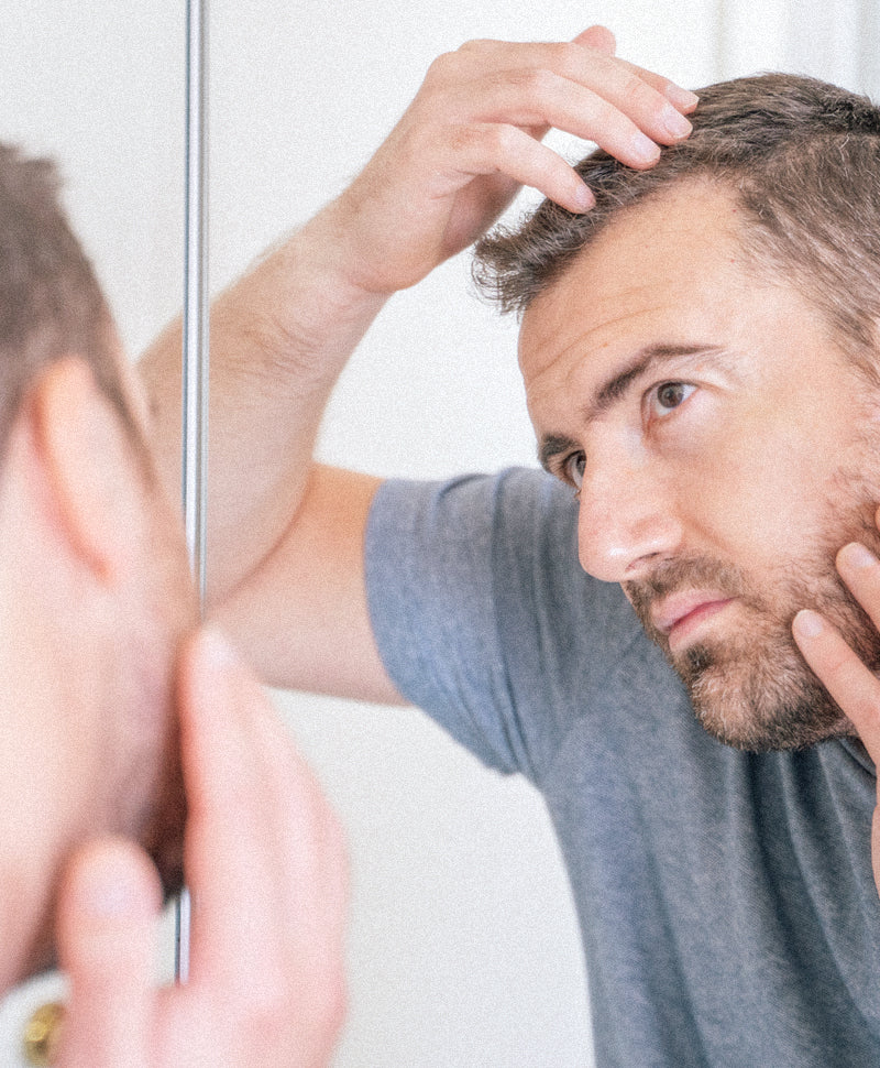 Mann prüft aufmerksam seine Kopfhaut vor dem Spiegel – Fokus auf Haarpflege und Haargesundheit.