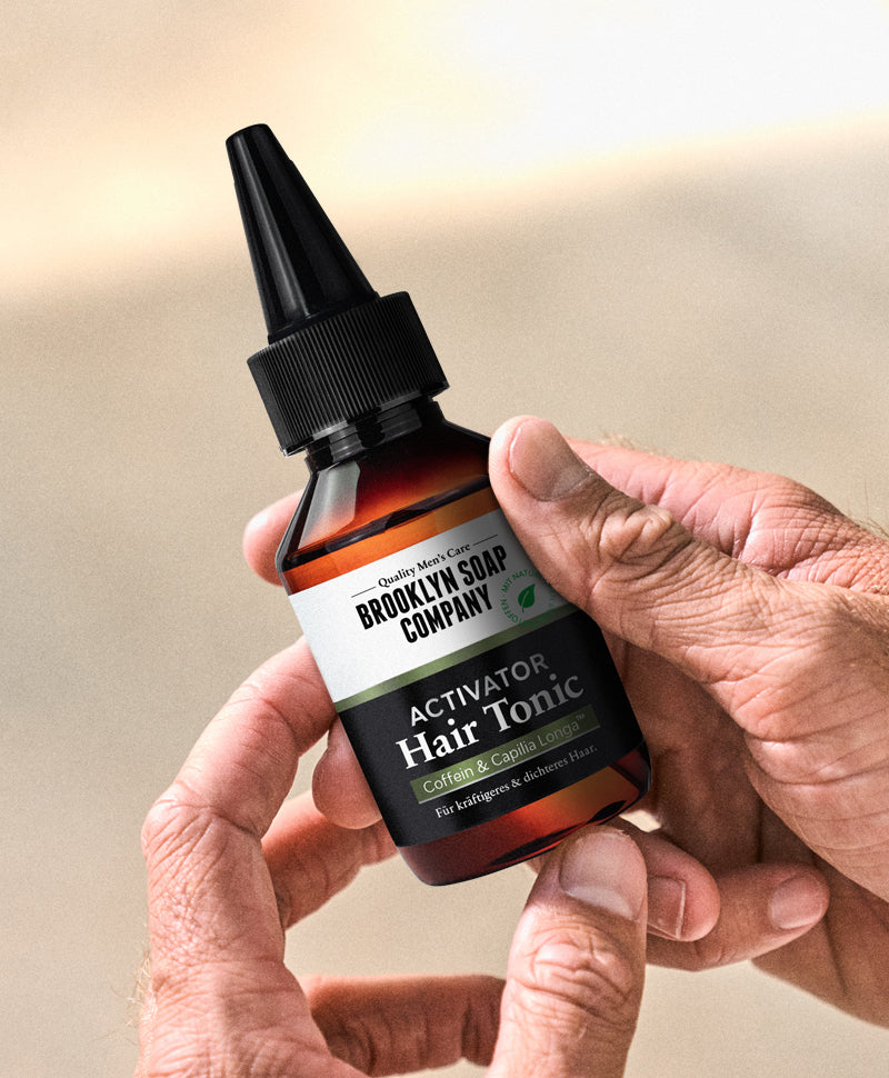 Eine Hand hält eine braune Flasche des Brooklyn Soap Company Activator Hair Tonics mit Applikator – für kräftigeres und dichteres Haar.