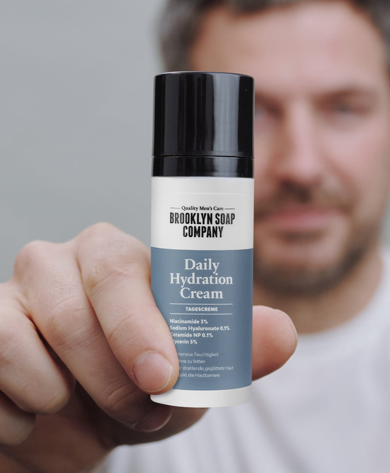 Ein Mann hält die Daily Hydration Cream von Brooklyn Soap Company in die Kamera – Tagescreme mit Niacinamide und Hyaluron für intensive Feuchtigkeitspflege.